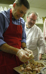 Steve Eiting, complete with hair net, gets a little instruction from Chef Matt Baker on how to place bacon-wrapped scallops onto skewers during a cooking class Saturday night at Haus der Eleganz in Minster. After three hours of the cooking class, Eiting and four other men served an elegant meal to their wives as a Valentine's Day gift. <br></br>dailystandard.com